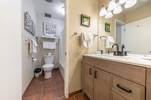 Une salle de bain avec des toilettes, un lavabo et un meuble de rangement. Des serviettes sont accrochées au mur et il y a une poubelle.