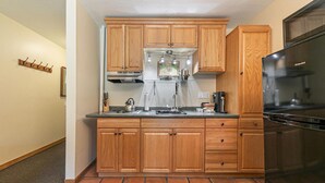 A compact kitchen with wooden cabinets, a stainless steel range hood, a built-in oven, and a black refrigerator. - Studio w/Kitchen 2nd Floor #217 at Donner Lake Village (Truckee)
