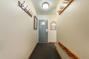Un couloir étroit doté d’un sol recouvert de moquette, une porte au fond et des crochets en bois fixés aux murs de part et d’autre.