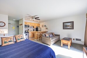 A bedroom with a bed, a sofa, a small table, a ceiling fan, and a kitchen area with wooden cabinets and appliances. - Cozy Studio w/ Partial Lake view #223 at Donner Lake Village (Truckee)