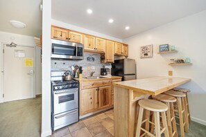 A modern kitchen with wooden cabinets, stainless steel appliances, a built-in oven, and a bar area with stools.