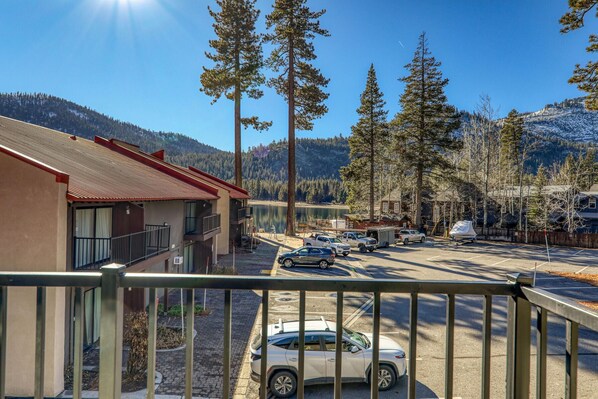 A hotel with a red roof, a parking lot with several cars, and a view of a lake and mountains in the background.