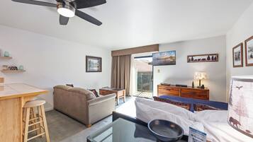 A hotel room with a bed, a sofa, a dining table, a ceiling fan, and a view of the outdoors.
