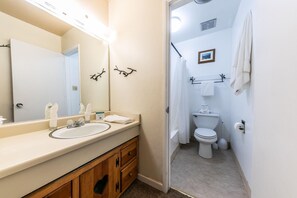 Un baño con lavamanos, espejo e inodoro. Hay toallas y artículos de aseo en la encimera.