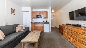 A compact living space with a kitchenette, a sofa, a wooden table, and a TV. - Cozy Studio #226 at Donner Lake Village (Truckee)