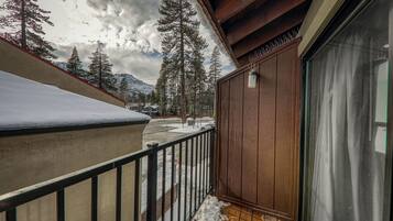 A balcony with a wooden railing, a glass door, and a view of snow-covered ground and trees.