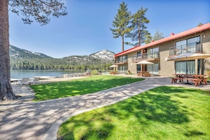 Un hotel frente al lago con un césped bien cuidado, mobiliario exterior y vistas al lago y a las montañas.