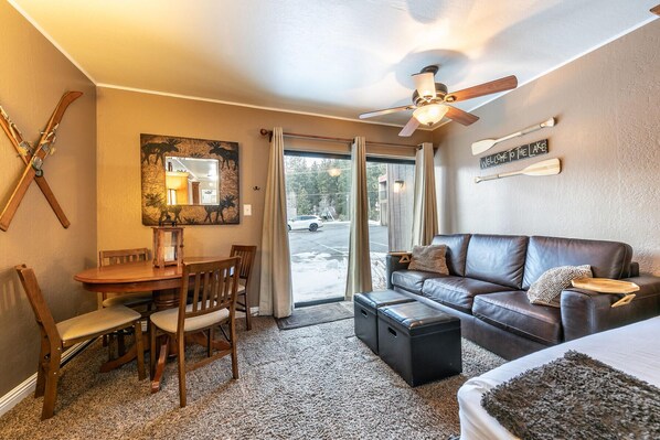A cozy room with a dining table, chairs, a leather sofa, a ceiling fan, and a large mirror.