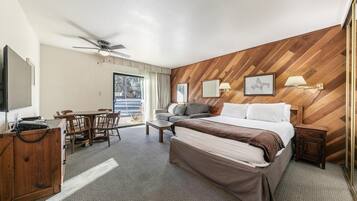 Habitación de hotel con cama, escritorio, silla, televisor y ventilador de techo.