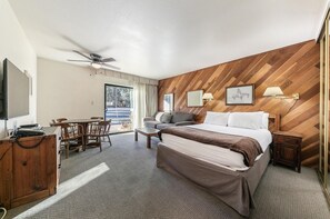 A hotel room with a bed, a desk with a chair, a television, and a ceiling fan.