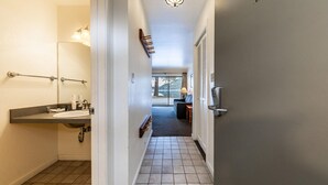 A hallway with a bathroom on the left, a door with a keypad lock on the right, and a view of a lake through a glass door.