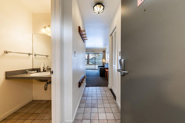 Um corredor com um banheiro à esquerda, uma porta com fechadura eletrônica à direita e vista para um lago através de uma porta de vidro.