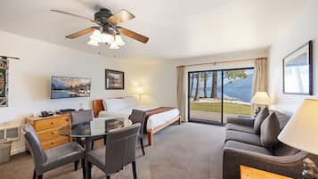 A hotel room with a bed, a sofa, a dining table with chairs, a ceiling fan, and a large window with a view of the outdoors.