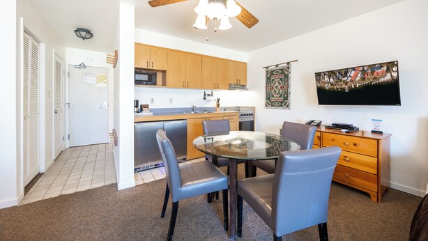 A compact kitchen with wooden cabinets, a microwave, and a dining area with a glass table and chairs.