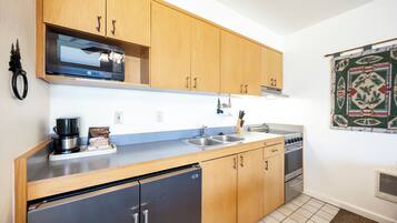 A compact kitchen with wooden cabinets, a built-in microwave, a stainless steel refrigerator, and a stove.
