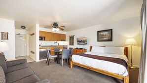 A hotel room with a bed, a desk, a chair, a sofa, a ceiling fan, and a lamp.