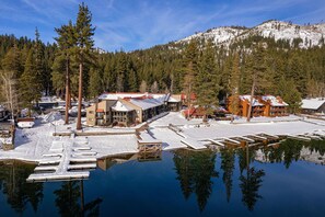 A lakeside lodge with multiple buildings, docked boats, and a snowy mountain backdrop.