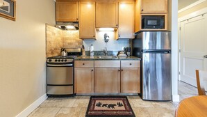 A compact kitchen with wooden cabinets, a stainless steel refrigerator, a microwave, a stove, and a sink.