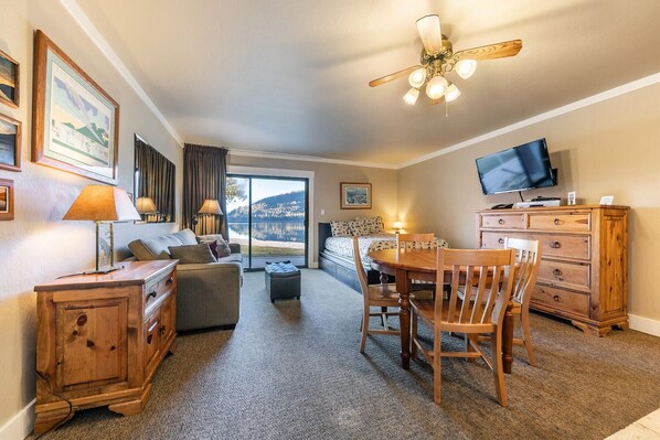 A cozy hotel room with a large window, a ceiling fan, a television, and a wooden dresser.