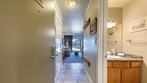 A hotel hallway with a door labeled "146", a bathroom with a sink and wooden cabinets, and a view of a balcony with a mountain in the background.