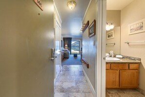 A hotel hallway with a door labeled "146", a bathroom with a sink and wooden cabinets, and a view of a balcony with a mountain in the background.