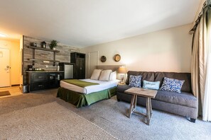 Une chambre d’hôtel compacte comprenant un lit, un canapé, une petite table, une kitchenette et une poubelle.