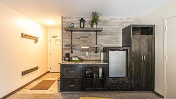 A compact hotel room with a kitchenette, a bed, a wardrobe, and a small seating area.