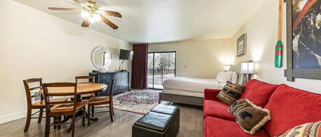 Une chambre d’hôtel compacte comprenant un coin repas, un lit, un canapé rouge et un ventilateur de plafond.