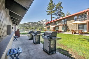 An outdoor patio with three barbecue grills, picnic tables, and a view of a mountain.