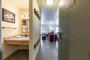 A hotel corridor with a bathroom on the left, a bed in the middle, and a door with the number 233 on the right.