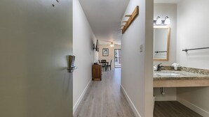 Een hal met een houten vloer, een deur links en een badkamer met een wastafel en spiegel rechts.