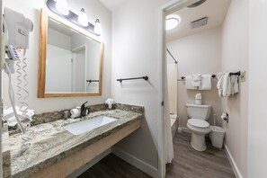 Une salle de bain avec un lavabo doté d’un plan de travail en granit, un miroir avec éclairage intégré, un porte-serviettes, des toilettes et un espace douche.
