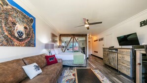 Une pièce confortable avec un lit, un canapé marron, une télévision et un ventilateur de plafond.