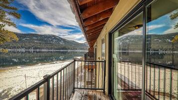 A wooden deck with a glass balustrade overlooking a lake and forested mountains.