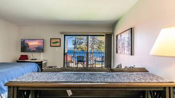 A hotel room with a bed, a desk, a chair, a TV, and a balcony with a view of the sea.