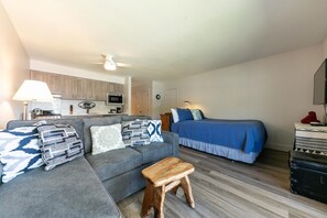 Un espacio habitable compacto con sofá, cama, taburete de madera y kitchenette.