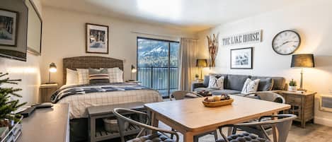 Una habitación de hotel acogedora con cama, una mesa de comedor y sillas. Cuenta con un balcón con vistas a las montañas.