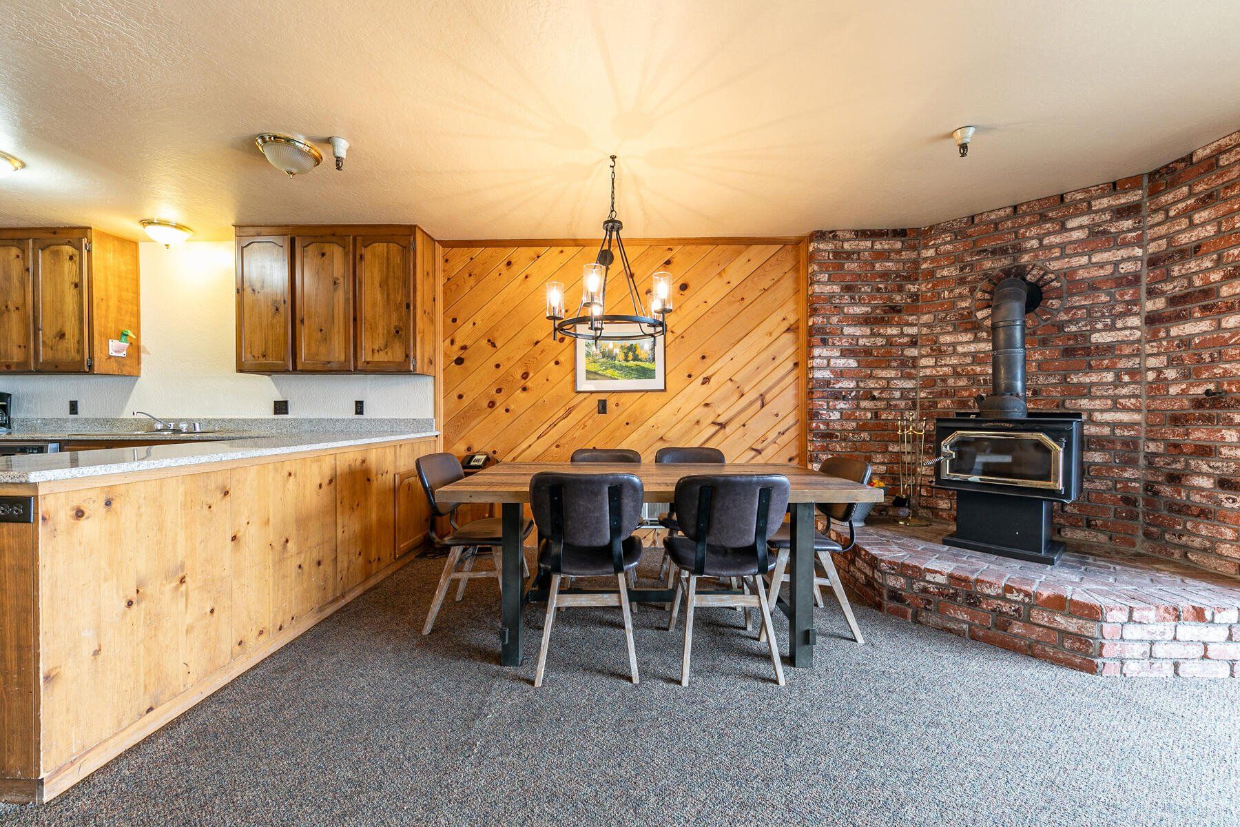 Eine Küche mit Holzschränken, einem Esstisch mit Stühlen, einer Hängelampe und einer Backsteinwand mit Holzofen.