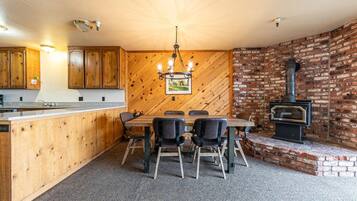 Eine Küche mit Holzschränken, einem Esstisch mit Stühlen, einer Hängelampe und einer Backsteinwand mit Holzofen.