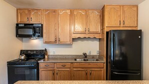 Une cuisine avec des meubles de rangement en bois, un micro-ondes noir, une cuisinière, un évier et un réfrigérateur noir.