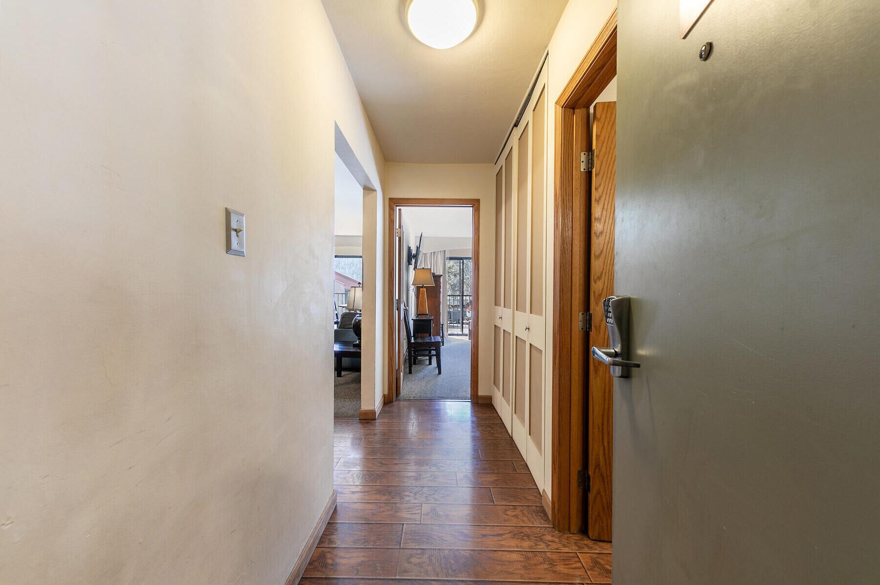 Un couloir étroit, doté d’un plancher en bois, mène à une pièce qui possède une porte.