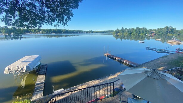 A calm lake with a wooden dock extending into the water, surrounded by greenery and a clear sky.