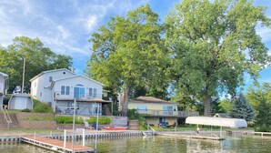 A lakeside property with a dock, a covered seating area, and a house with a balcony overlooking the water.