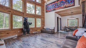 A spacious room with large windows, a bear statue, a dining area, and a staircase.