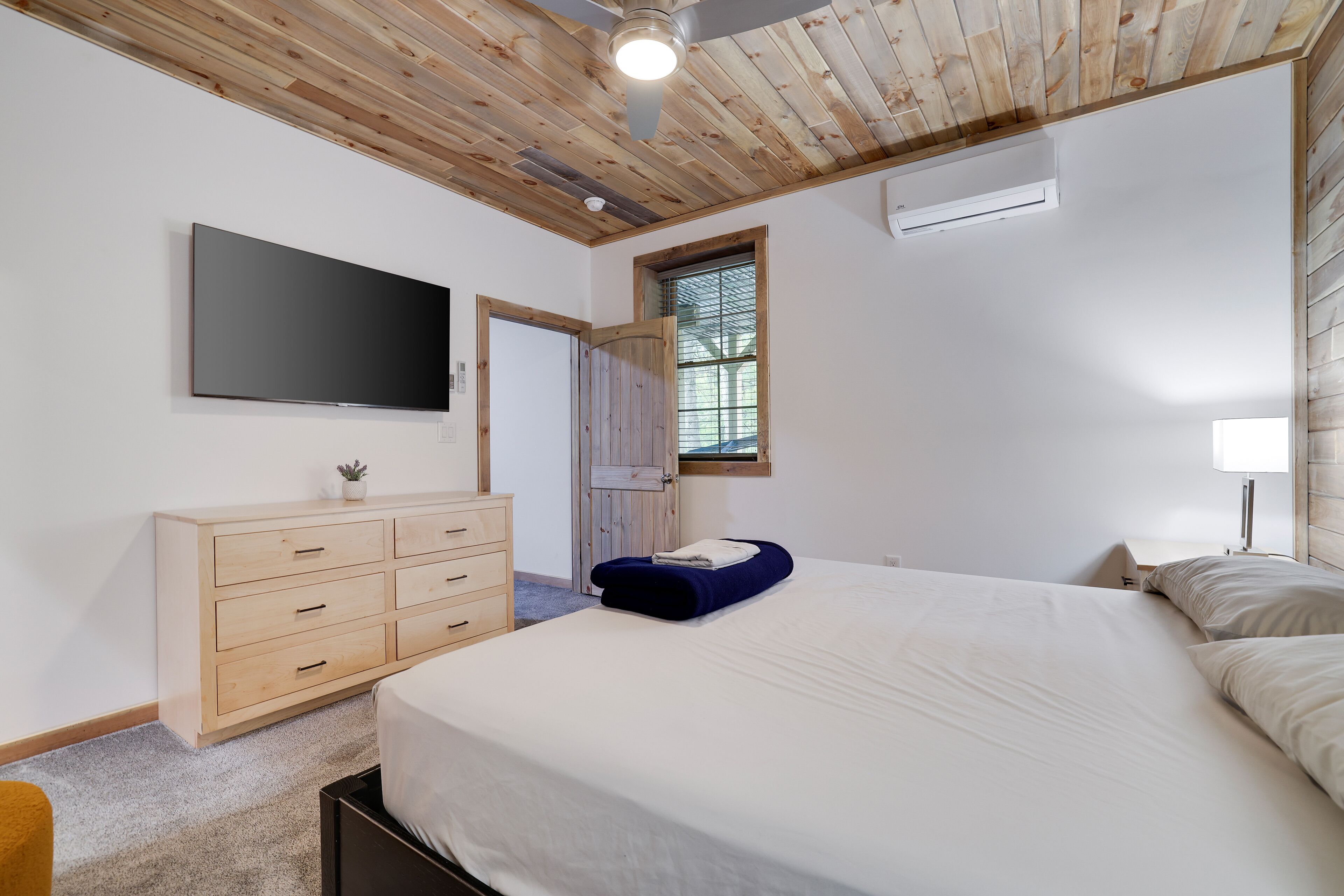 A bedroom with a bed, a dresser, a TV, a window, and a ceiling fan.