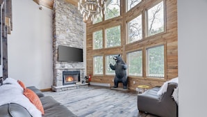 A cozy living room with a stone fireplace, a bear statue, and large windows.