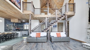 A spacious living area with a high ceiling, a staircase, and a kitchen in the background.