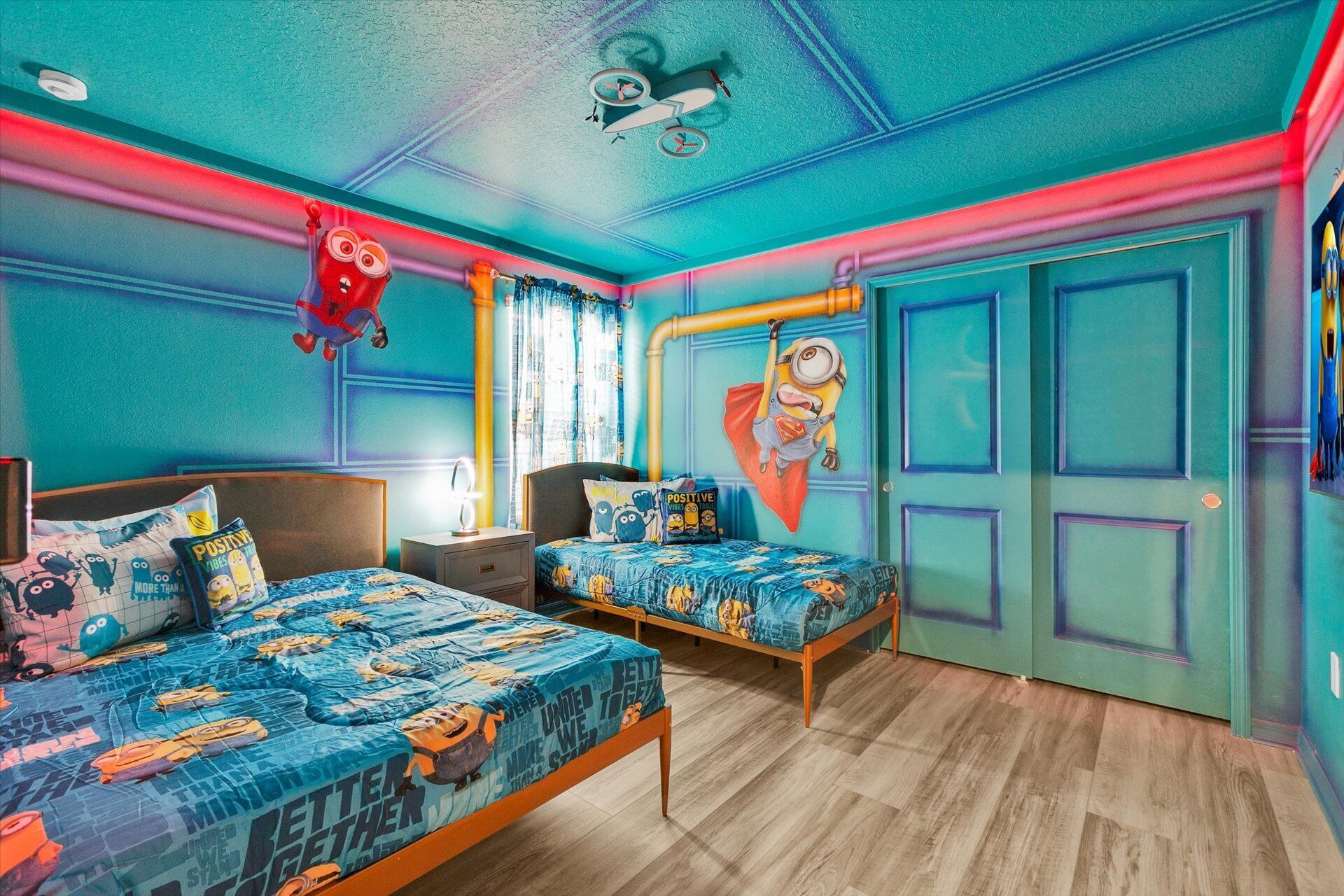 A bedroom with two beds, a ceiling fan, and a Minion-themed bedspread.