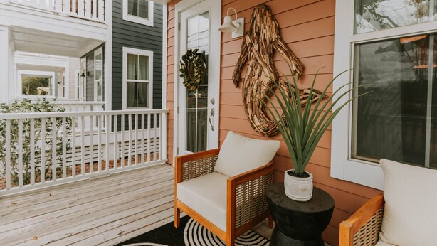 A wooden deck with a white railing, a wicker chair with a cushion, and a potted plant. - Mermaid's Muse - Includes GOLF CART! Close to beach & downtown Ocean Springs! (Ocean Springs)