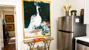 A kitchen with a stainless steel refrigerator, a gold-framed painting of a peacock, and a glass cart with kitchen items. - Mermaid's Muse - Includes GOLF CART! Close to beach & downtown Ocean Springs! (Ocean Springs)